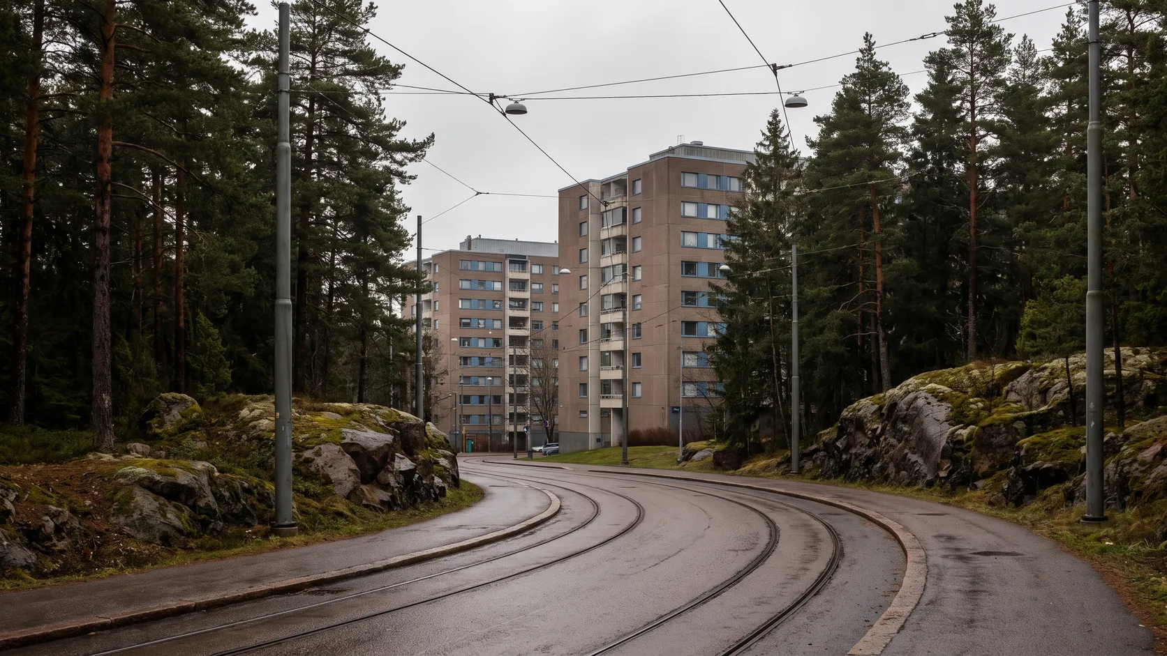 Höghus på en skogsklädd kulle och spårvagnsspår i Angered.