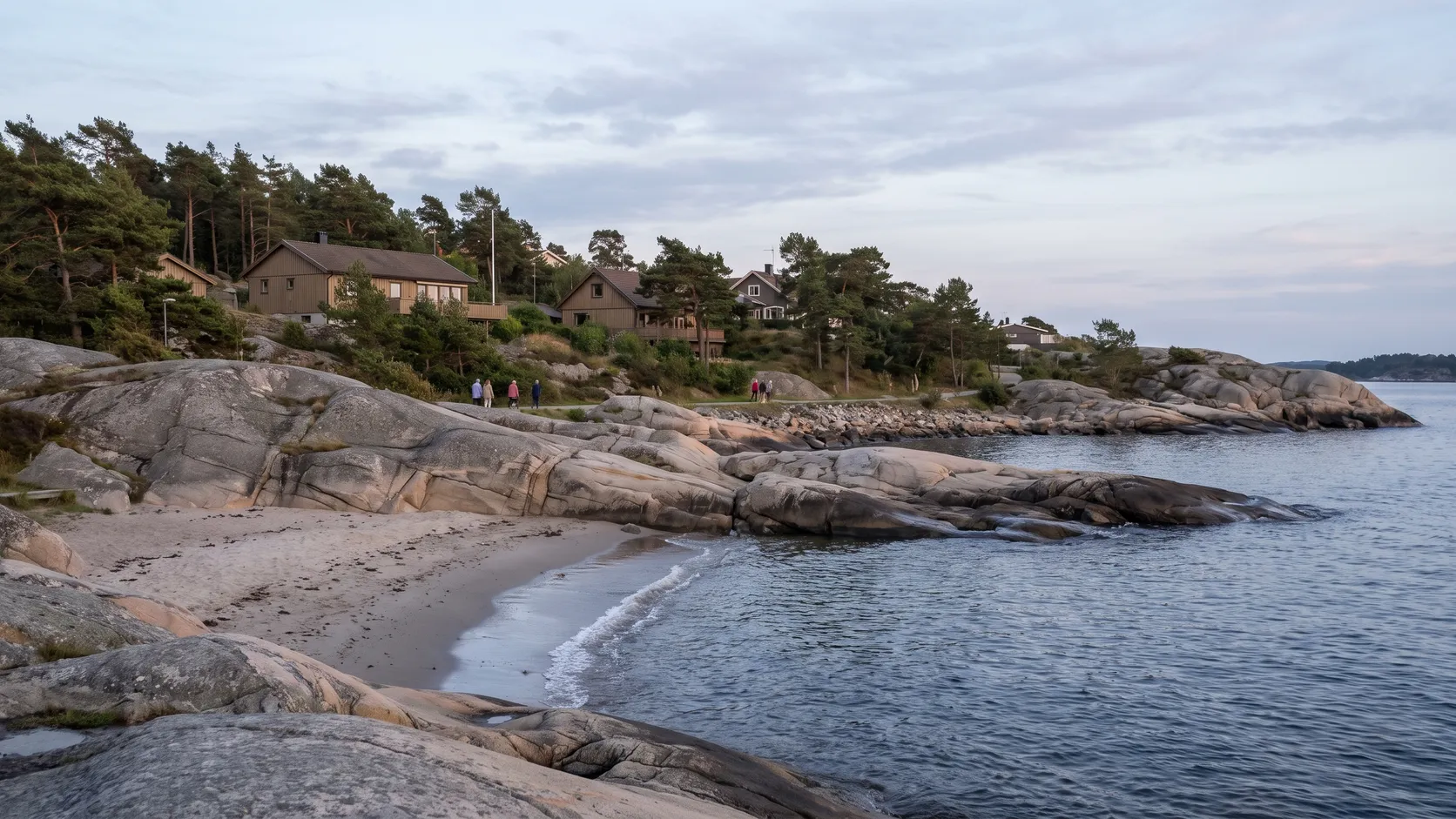 Klippor och en liten sandstrand vid havet med villor i Askim.